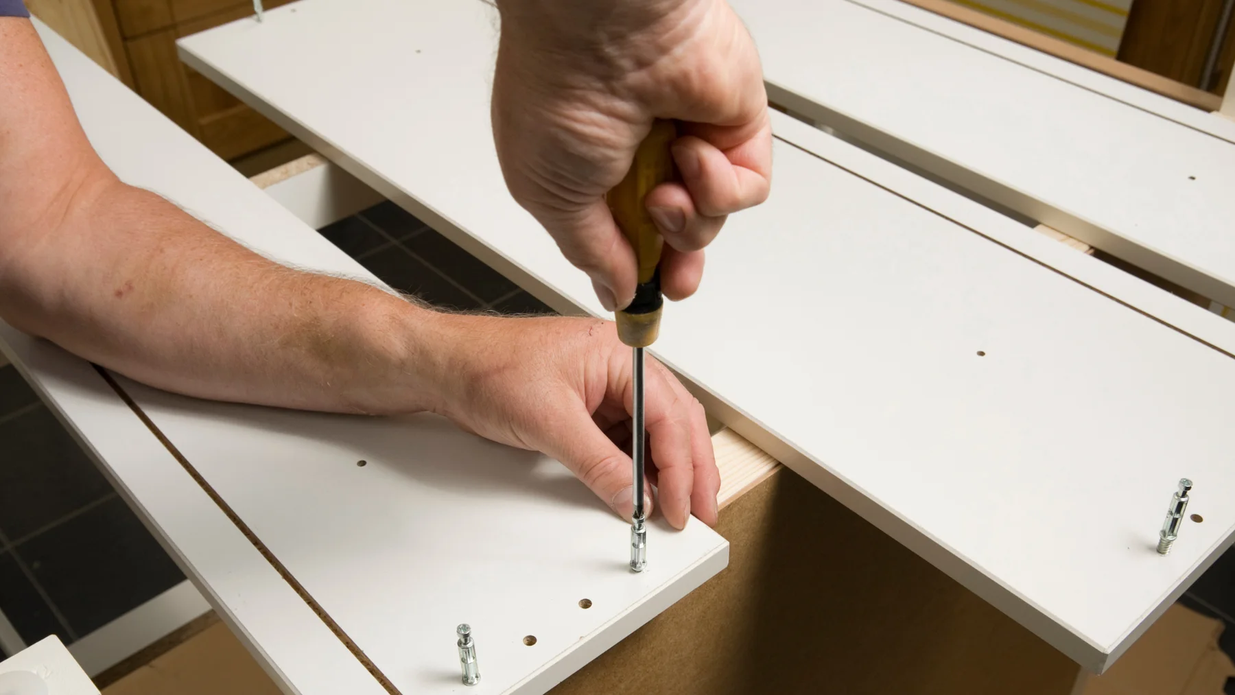 Illustrative close-up of hands fastening a furniture panel during assembly
